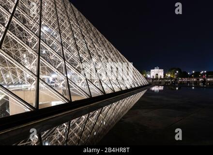 At night, illuminated glass pyramid in the Louvre is reflected in the water, further back you can see the Arc de Triomphe du Carrousel, Paris, France, Europe