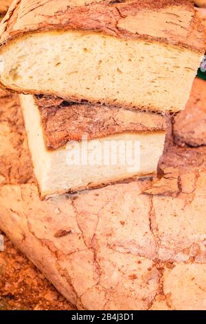 Europe, Italy, Piedmont, Cannobio. Fresh stone oven bread a trader slices on the weekly market of big loaves. Stock Photo