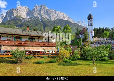 Inn with sun terrace and village church above the cemetery against Waxenstein 2277m Riffelwand and Zugspitze 2962m in the Wetterstein Mountains, Grainau, Werdenfelser Land, Zugspitzland, Upper Bavaria, Bavaria, Germany Stock Photo