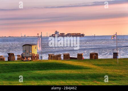 Grass beach with beach chairs on the Wadden Sea and container ship in the evening sun, North Sea resort Wremen, Land Wursten, Weser estuary, North Sea, North Sea coast, National Park Lower Saxony Wadden Sea, Lower Saxony, Germany Stock Photo
