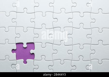 A white puzzle is placed on a purple background and is missing a piece Stock Photo