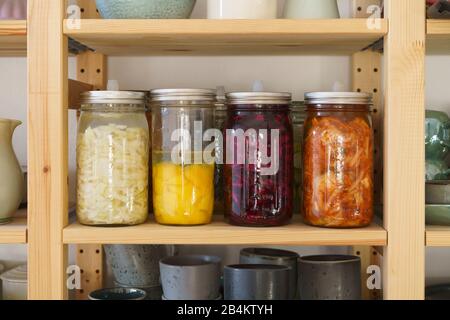 White cabbage, kimchi, red cabbage and kale fermented, pickled in preserving jars on the storage shelf Stock Photo