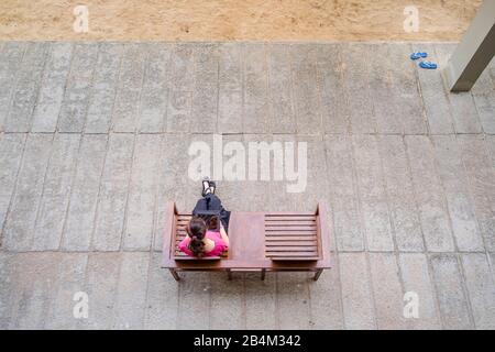 a young woman with tablet computer sitting on a wooden bench on a plat, taken from above Stock Photo