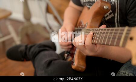Cropped shot of male musician practicing guitar while siting on chair in music instrument Stock Photo