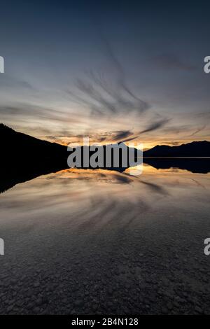 The Simetsberg unfolds angel wings, reflected in the water of the Walchensee at sunset. Cloud formation in the form of a wing. Stock Photo