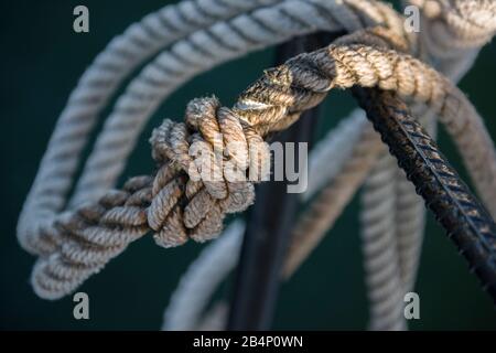 Knot in a maritime white rope around rebar in a dark green background Stock Photo