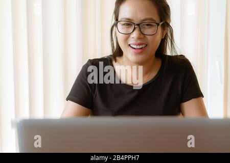 happy woman using laptop. Young Asian woman sitting at home and working on laptop Stock Photo