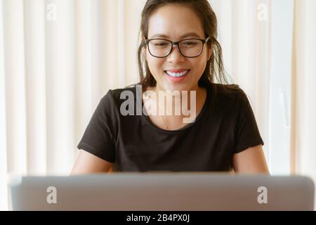 happy woman using laptop. Young Asian woman sitting at home and working on laptop Stock Photo