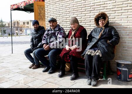 Four uzbek men and women sitting on a porch and chatting in old town of Bukhara, Uzbekistan Stock Photo