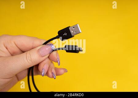 Micro USB cable in hand close-up on yellow background Stock Photo