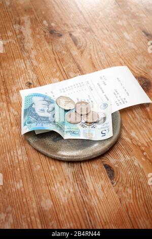 A bill and a tip left on a table in a restaurant with English money Stock Photo