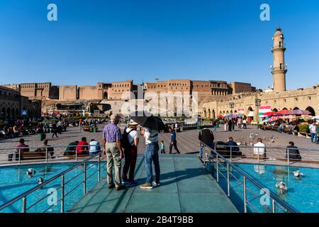 Iraq, Iraqi Kurdistan, Arbil, Erbil. In the middle of the fountain on the park Shar a group of three peaople are chatting. One is under an umbbrella. Stock Photo