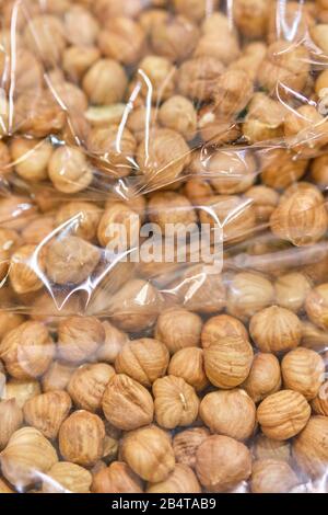Packing from a transparent bag with peeled hazelnuts. Close up. Vertical.