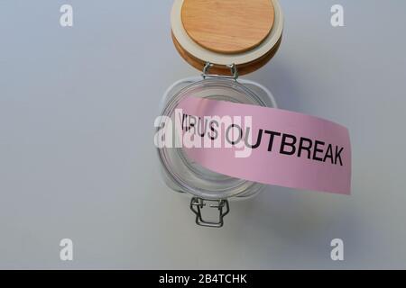 Closeup words VIRUS OUTBREAK on pink paper in open glass bottle placed on wooden table, epidemic concept, let the genie out of the bottle concept Stock Photo