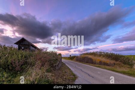 Road passage through dike at sunset under beautiful clouded sky. Usquert, Groningen, Netherlands Stock Photo