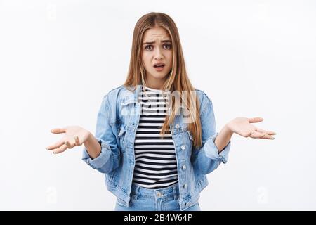 Why you acting like this. Troubled and worried, confused young blond woman shrug with hands spread sideways, need answers, standing clueless and Stock Photo