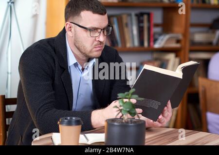 Man reading book and drinking coffee in a cafe with many books on a background Stock Photo