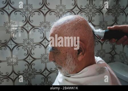 Very Old, White Haired, Bald Man Gets Haircut In Old Vintage Bathroom (retro exotic look) Stock Photo