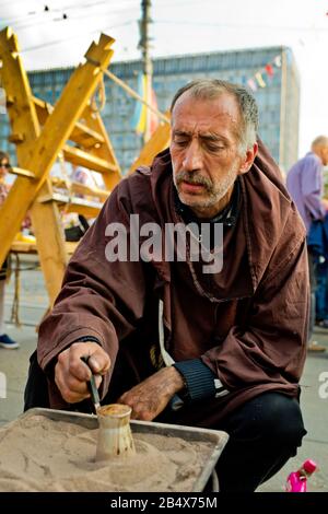Vinnytsia Ukraine - September 09, 2017: Birthday of the city of Vinnytsia. A man in a brown hoodie is brewing coffee on the sand. Stock Photo