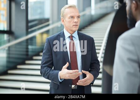 Horizontal medium porrait of mature Caucasian businessman standing in front of his unrecognizable colleague telling something to him Stock Photo
