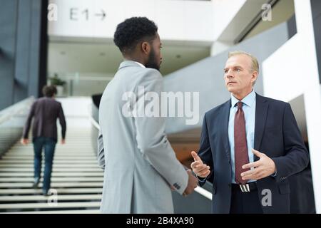 Horizontal low angle shot of two modern businessmen standing in front of each other discussing something Stock Photo