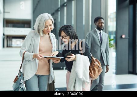 Two Asian women of different age standing in airport hall checking their documents, horizontal shot Stock Photo