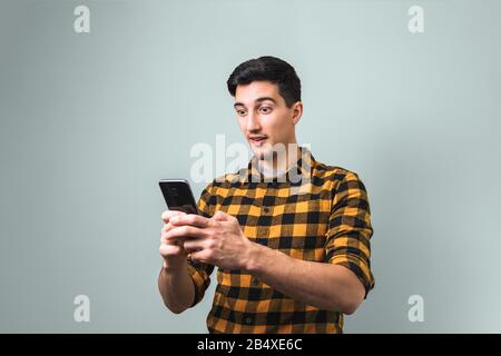 unbelievable happy news. surprised man in yellow shirt holding a phone on grey background Stock Photo