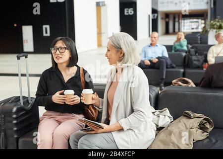 Senior Asian woman and her daughter spending time together in departure lounge drinking coffee while waiting for flight Stock Photo
