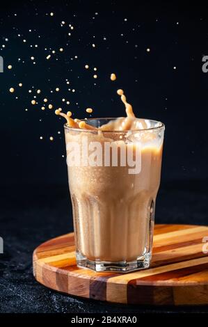 Iced Coffee with Splash in Tall Glass on Dark Background. Concept Refreshing Summer Drink. Stock Photo