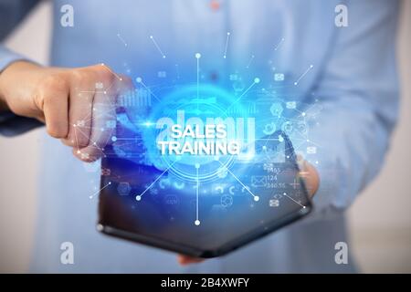 Businessman holding a foldable smartphone with SALES TRAINING inscription, new business concept