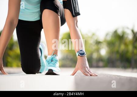 Front view of athletic women in running start pose on running track in the garden street. Sport and running concept. Stock Photo