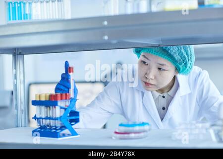 Horizontal medium close-up shot of young female Asian laboratory scientist taking out test-tube with some liquid Stock Photo