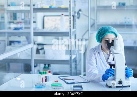 Horizontal shot of chemical industry worker sitting alone in modern laboratory using microscope, copy space Stock Photo