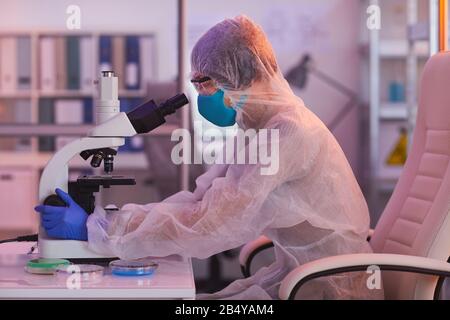 Horizontal side view shot of unrecognizable laboratory scientist working on new vaccine using microscope, purple light Stock Photo