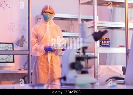 Unrecognizable female medical scientist wearing protective uniform holding test-tubes with liquids looking at camera, horizontal medium long shot, cop Stock Photo