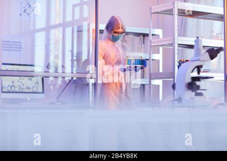 Unrecognizable female medical scientist wearing protective uniform carrying test-tubes with liquids, horizontal shot, copy space Stock Photo