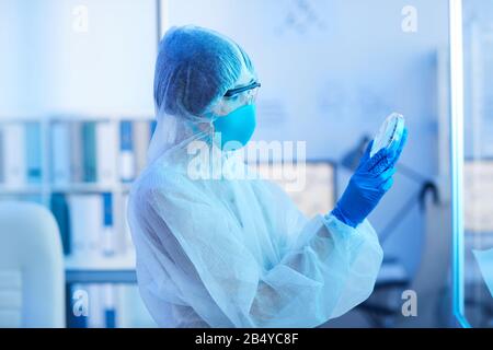 Horizontal side view shot of unrecognizable medical laboratory scientist holding petri dish with virus specimen looking at it Stock Photo