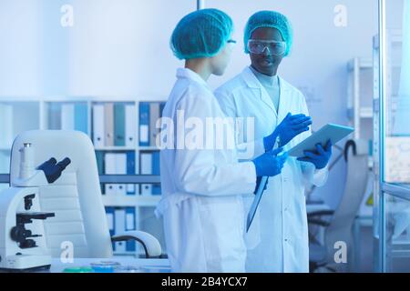 Horizontal medium long shot of two young man and woman working in laboratory together discussing something, copy space Stock Photo
