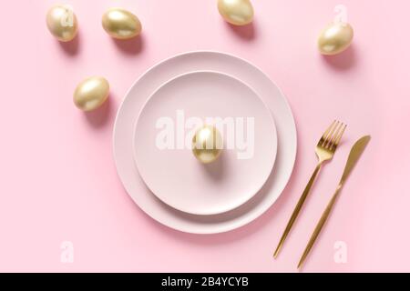 Easter table setting decorated golden eggs on pink table. Elegance dinner. Top view. Stock Photo