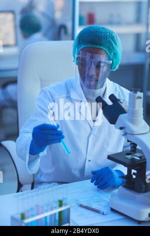 Vertical medium high angle shot of young male medical scientist holding test-tube with blue liquid doing laboratory tests Stock Photo