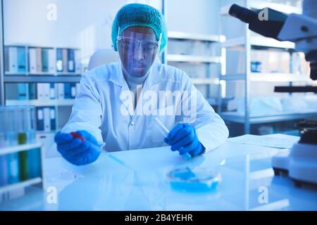 Professional pharmacologist sitting at desk working on new medication in modern laboratory, horizontal portrait Stock Photo