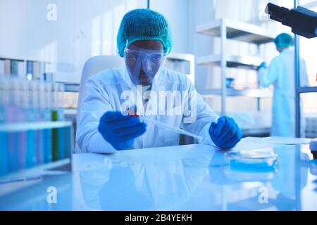Young male pharmacologist sitting at table working on new medication in modern laboratory, horizontal portrait Stock Photo