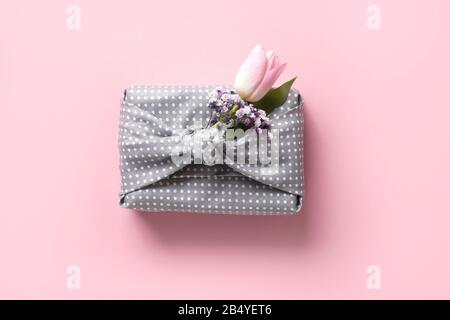 Spring eco-friendly gift wrapped in grey textile with flowers decor on pink. Sustainable gift. Zero waste. Easter holiday. Traditional Japanese Furosh Stock Photo