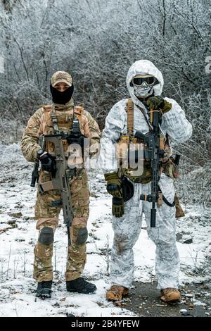 Two men in camouflage white, green uniform with machineguns. Soldiers with muchinegun in the winter forest. Stock Photo