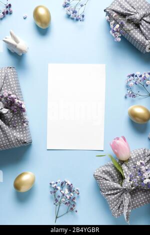 Easter frame of fresh flowers, golden eggs, presents and bunny on blue background. Top view with copy space. Happy Easter holiday. Vertical greeting c Stock Photo