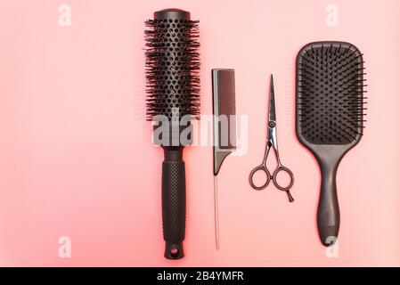Professional black combs and scissors. Hairdresser tools on a pink pastel background. Different hairbrushes for different purposes. Stock Photo