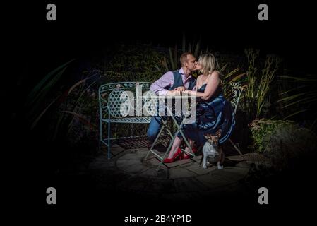 Quorn, UK - Aug 2019: Couple kissing on a garden bench at night, dog in forground Stock Photo