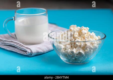 Fresh cottage cheese in a transparent bowl with a spoon with a glass of kefir on a blue background. Fermented foods. Good bacteria for health. Copy sp Stock Photo