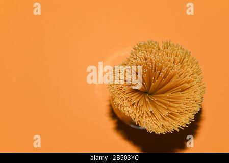 top view of yellow uncooked spaghetti pasta on a orange background, shooting with flash hard light, copy space for culinary recipe text or restaurant Stock Photo