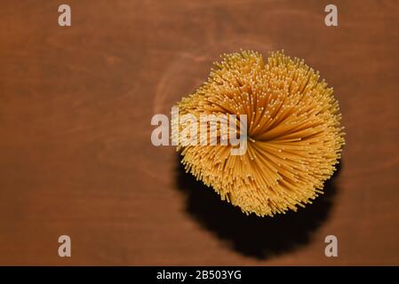 top view of yellow uncooked spaghetti pasta on a brown wooden table, shooting with flash hard light, copy space for culinary recipe text or restaurant Stock Photo